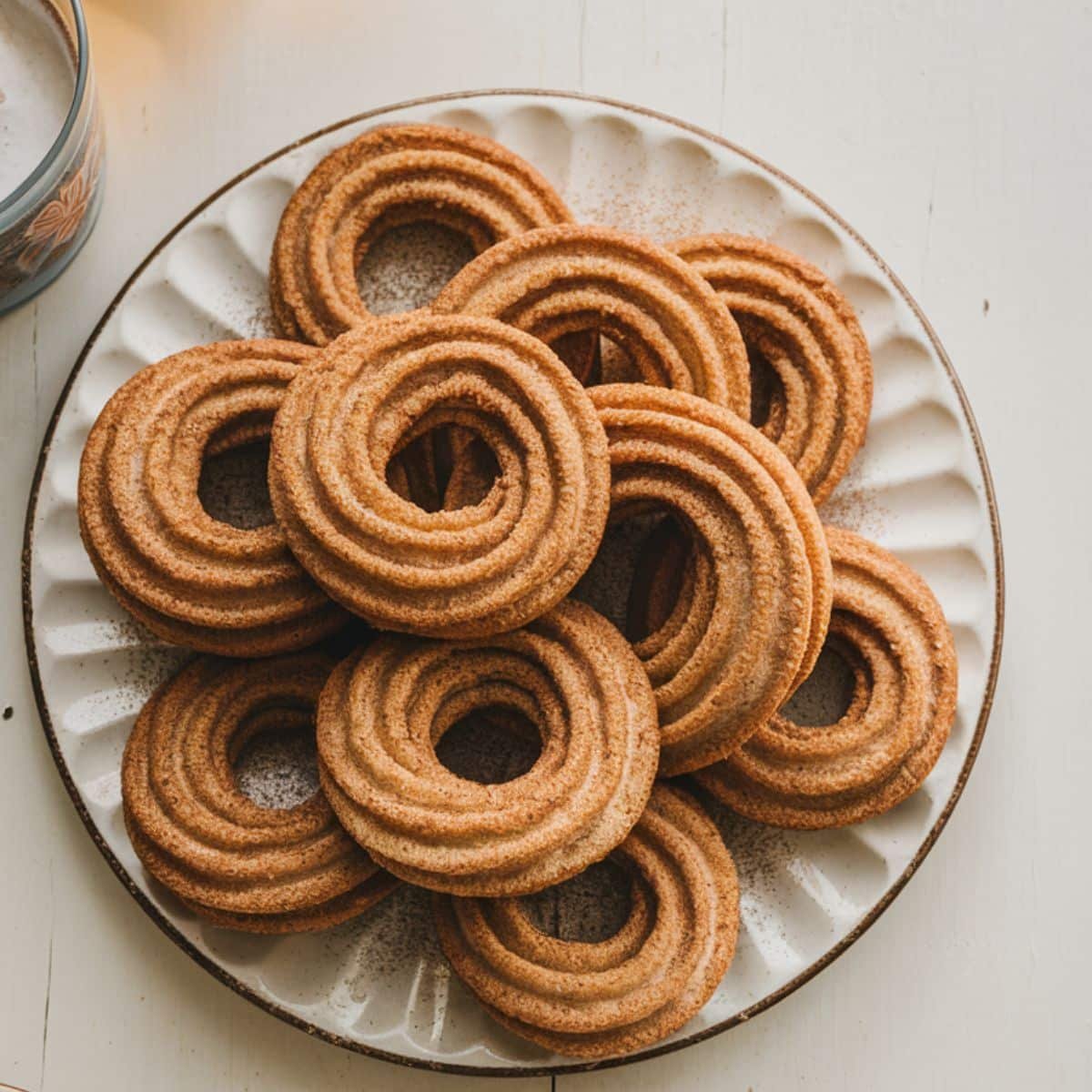 Freshly baked churro cookies dusted with cinnamon sugar on a white plate, placed on a kitchen counter.