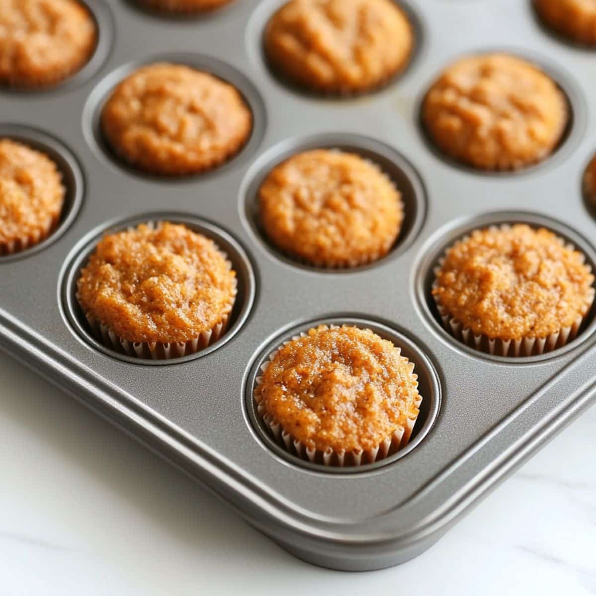 Mini carrot cupcakes cooling in tin on counter	