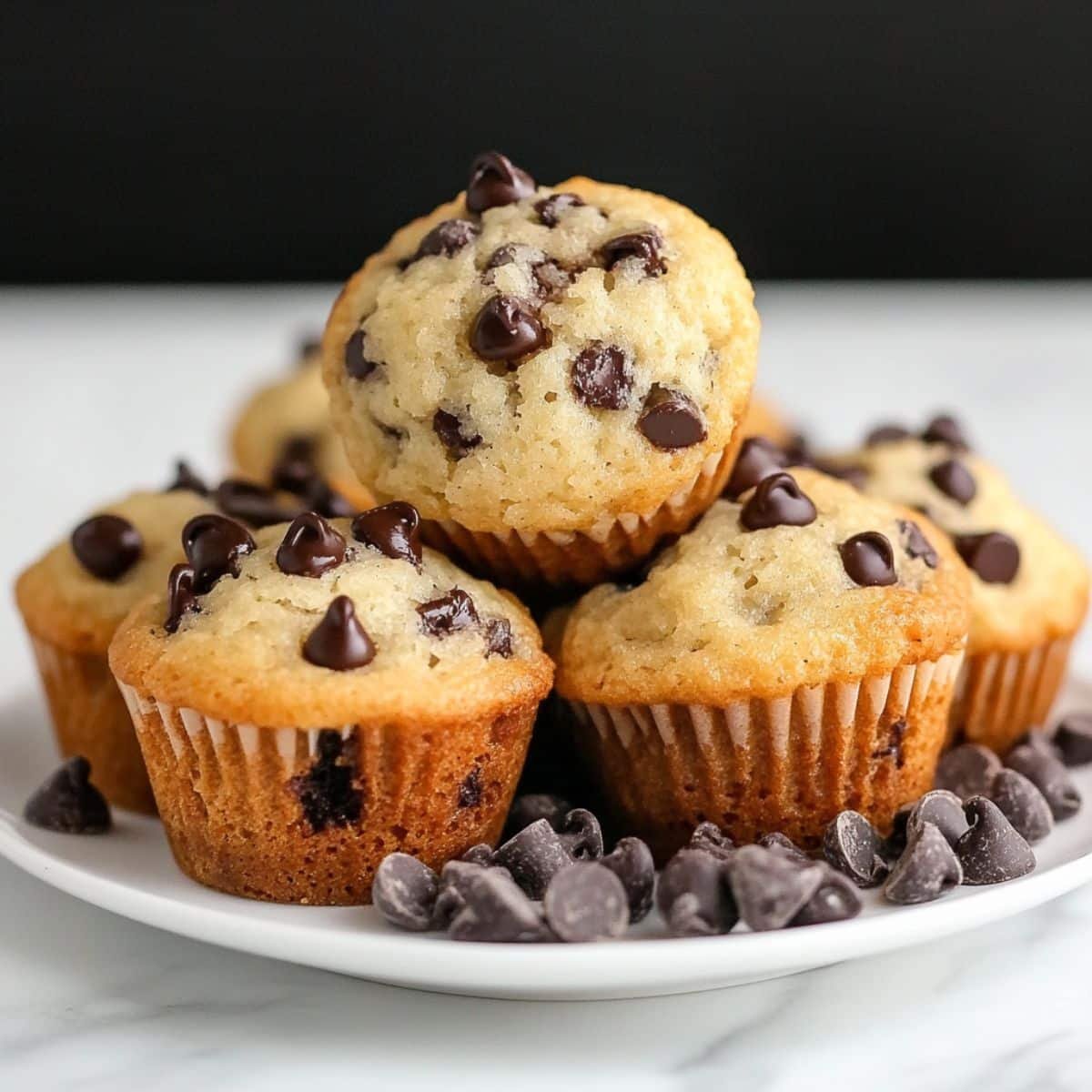 Freshly baked mini chocolate chip muffins stacked on a white plate	