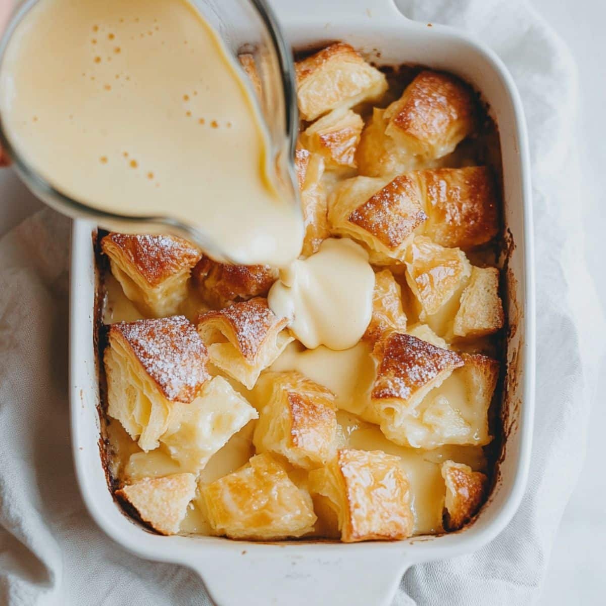 Croissant pieces soaked with custard in a baking dish.	
