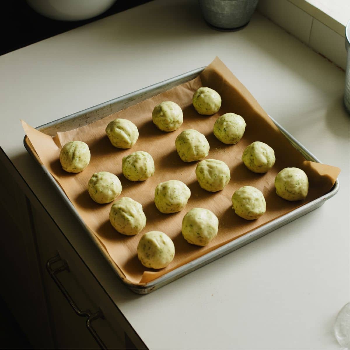 Key lime cookie dough balls spaced on a parchment-lined baking sheet	