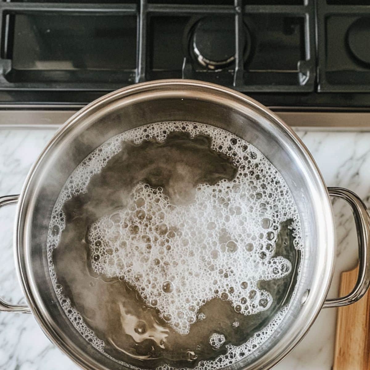 Baking soda water boiling in a large pot on stovetop. Marble counter and dough visible nearby