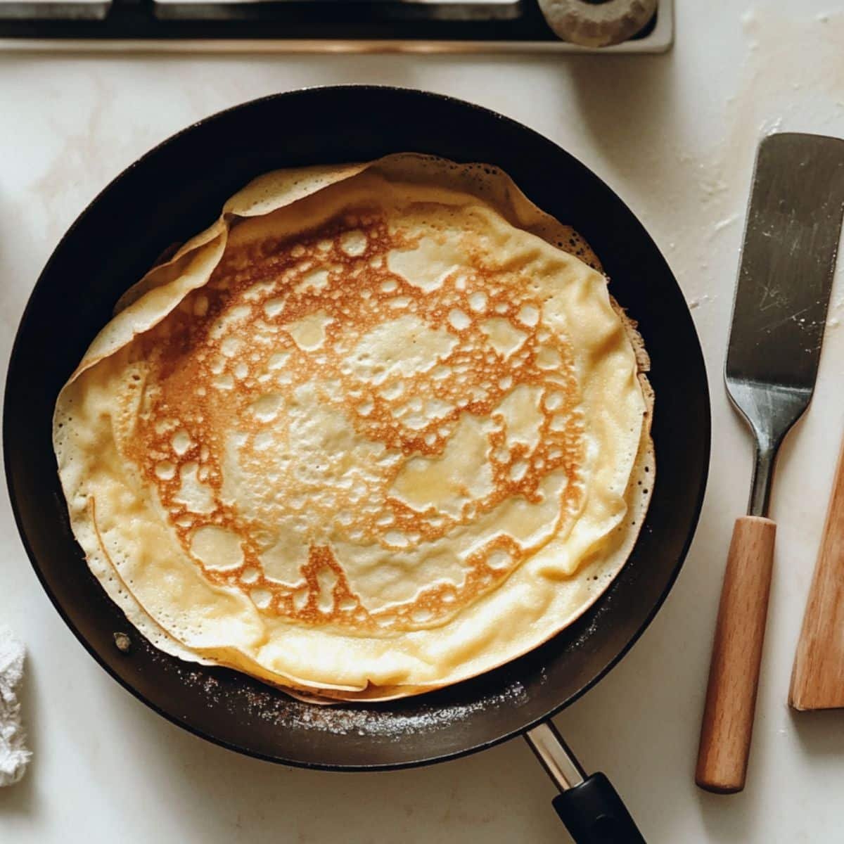 Thin gluten free crepes cooking in a skillet with lightly golden edges.