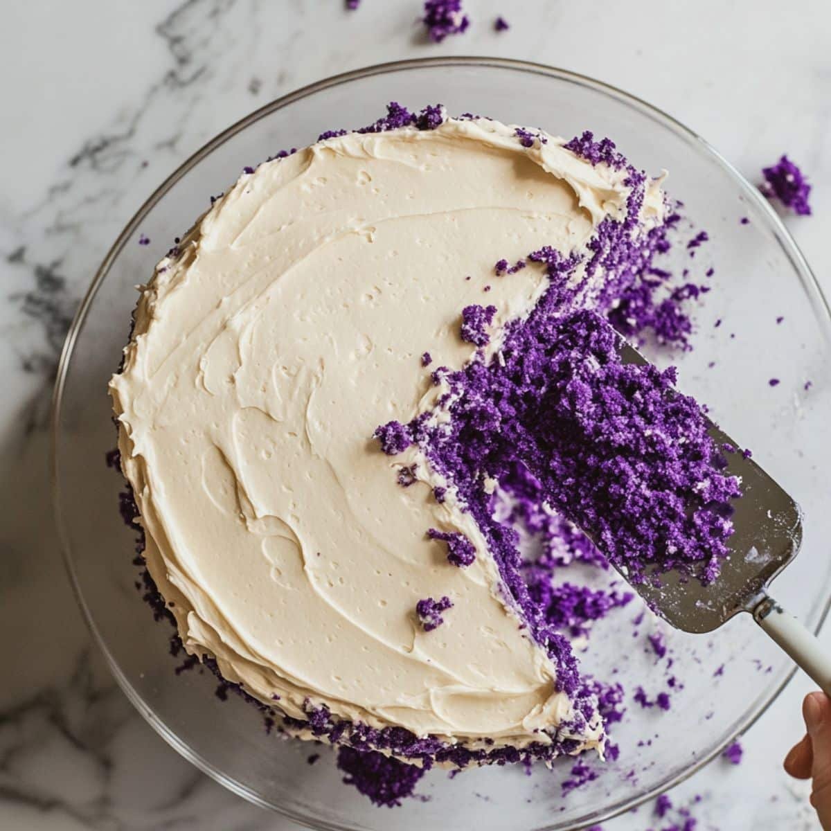 Frosting a vibrant ube layer cake with cream cheese on white plate. Overhead view with crumbs visible.