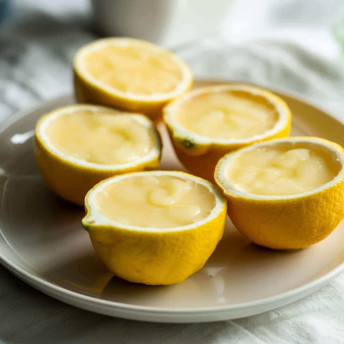 Unchilled lemon posset cream in lemon halves resting on a plate before setting	