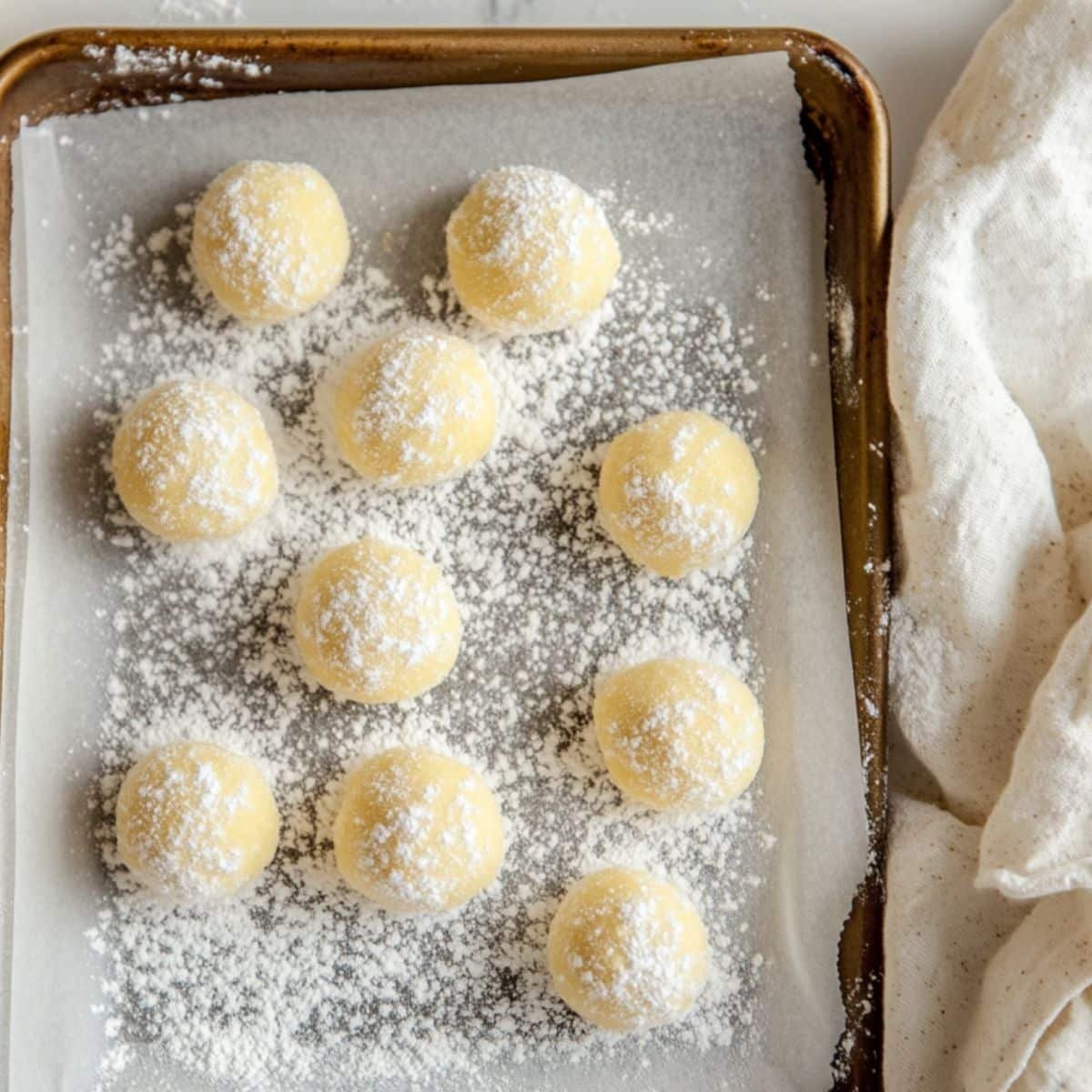 Lemon cookie dough balls coated in powdered sugar, ready to bake