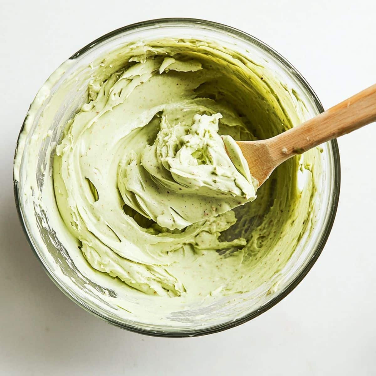 Creamy pistachio cheesecake filling in a mixing bowl with spatula	