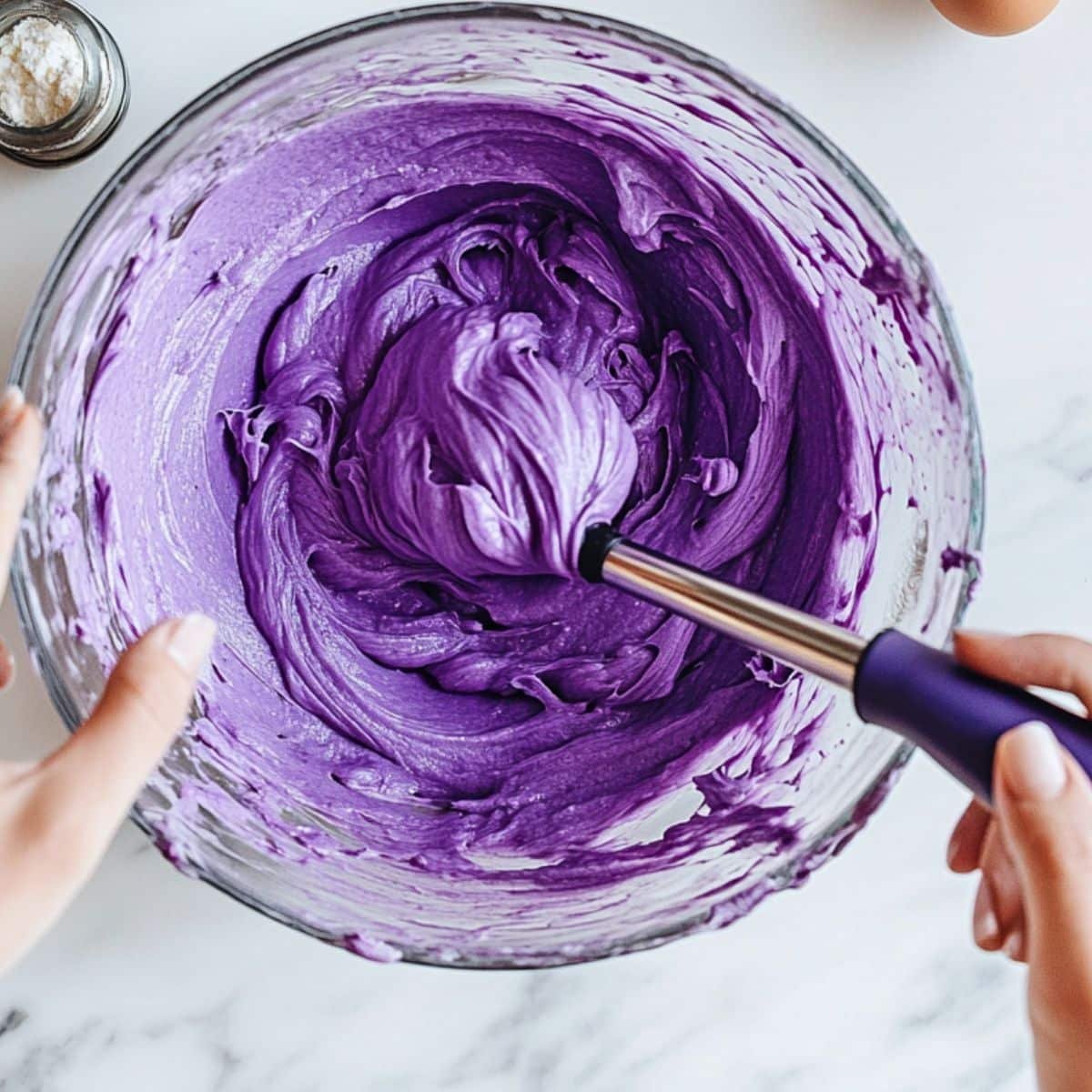 Overhead shot of smooth purple ube cake batter in a mixing bowl. Spatula and mixer nearby on white counter.