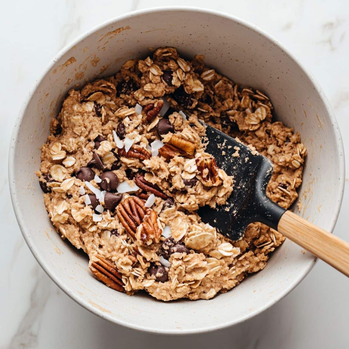 Cookie dough being mixed with oats, chocolate, pecans, and coconut	
