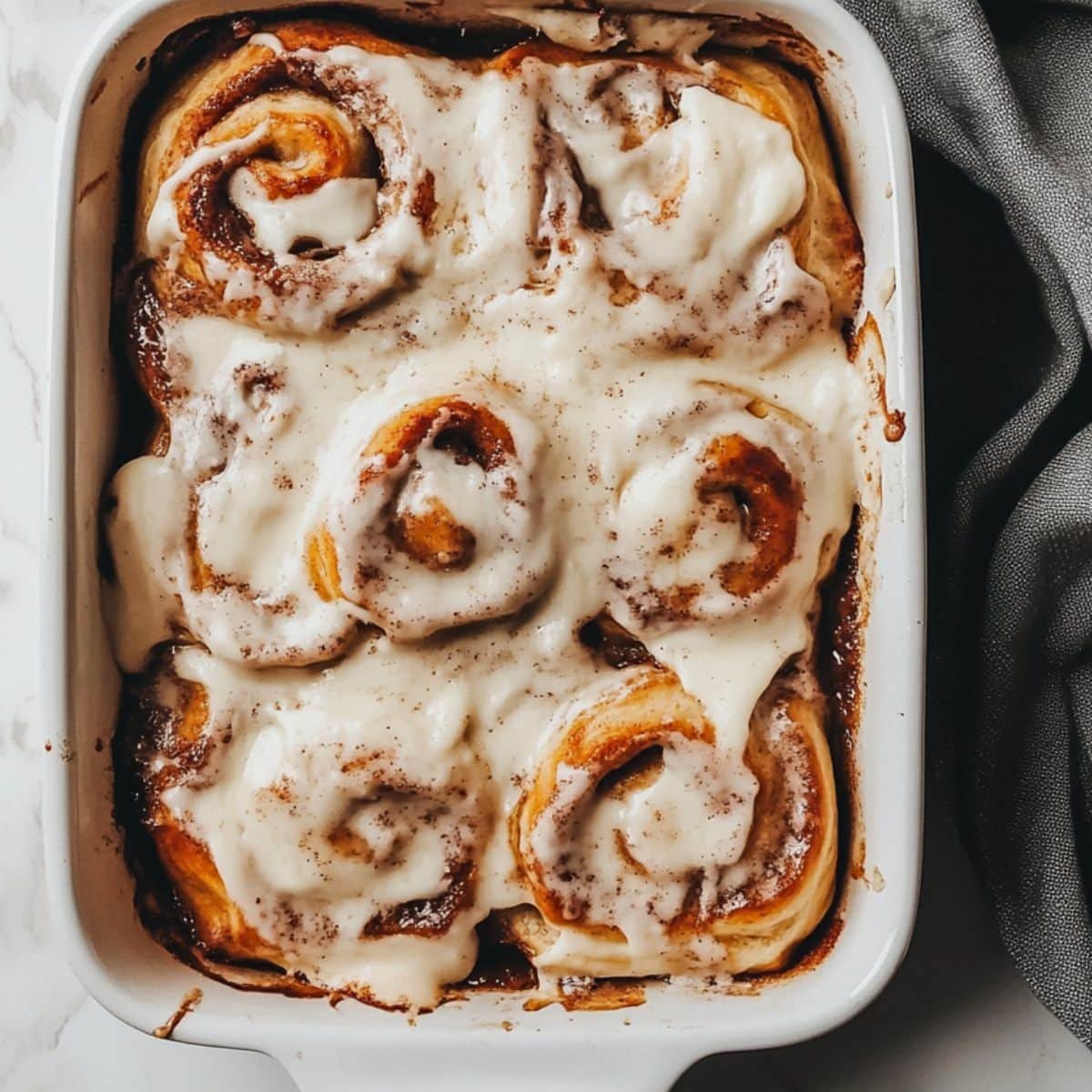 Golden sourdough discard cinnamon rolls with melting frosting on a white counter. A cozy homemade treat taken overhead in natural light.