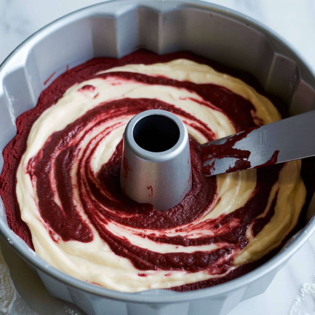 Swirling cream cheese filling into red velvet batter in bundt pan	