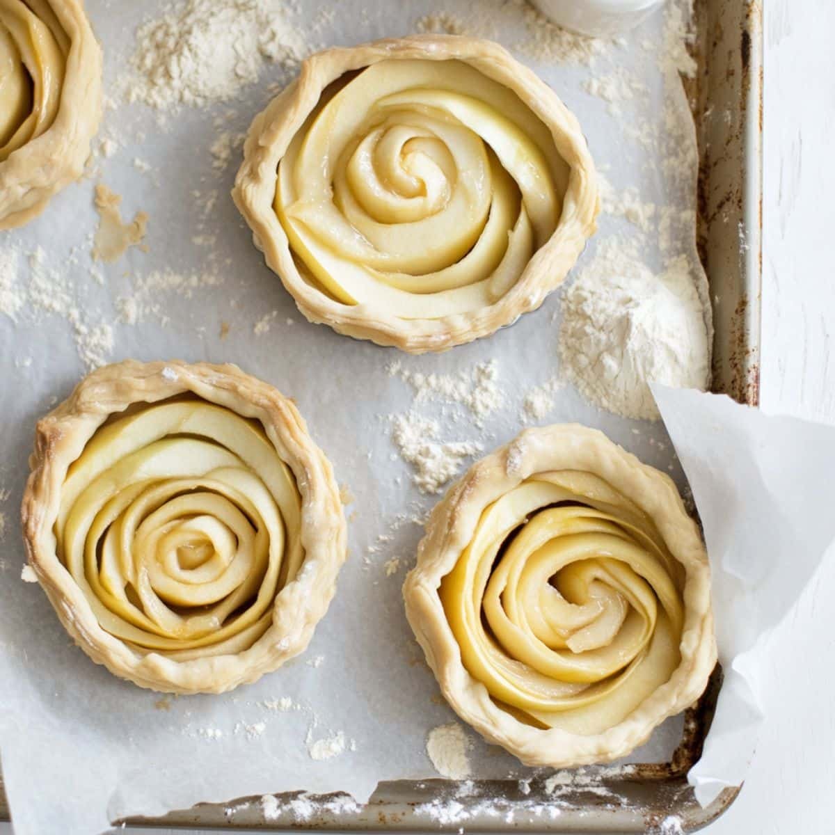 Unbaked apple tarts with folded edges and spiraled apples on a tray