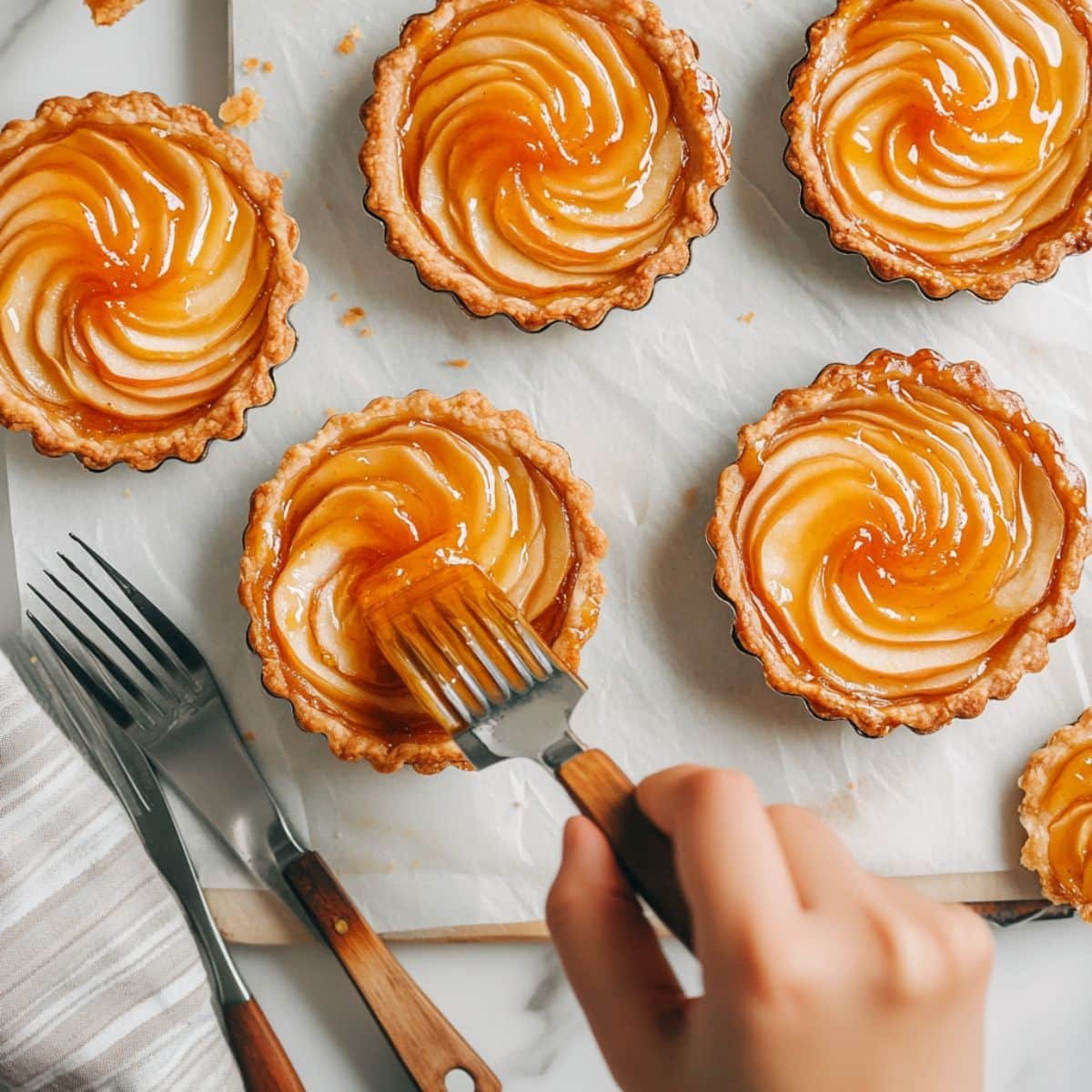 Brushing warm apple tarts with glaze before serving