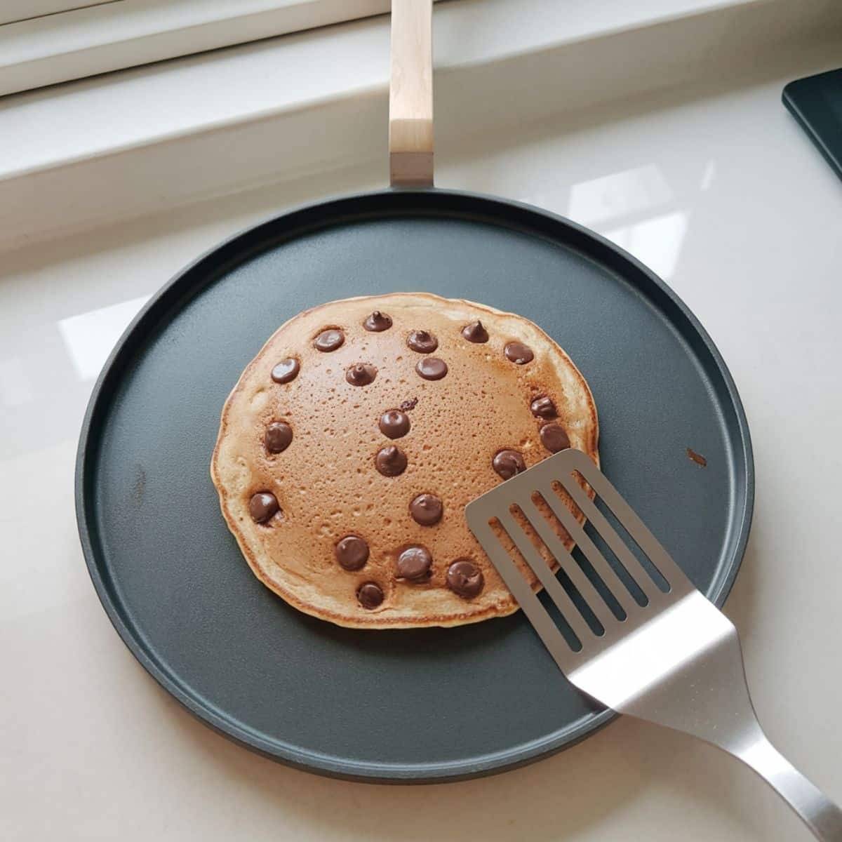 Chocolate chip pancakes cooking on griddle with bubbles forming	