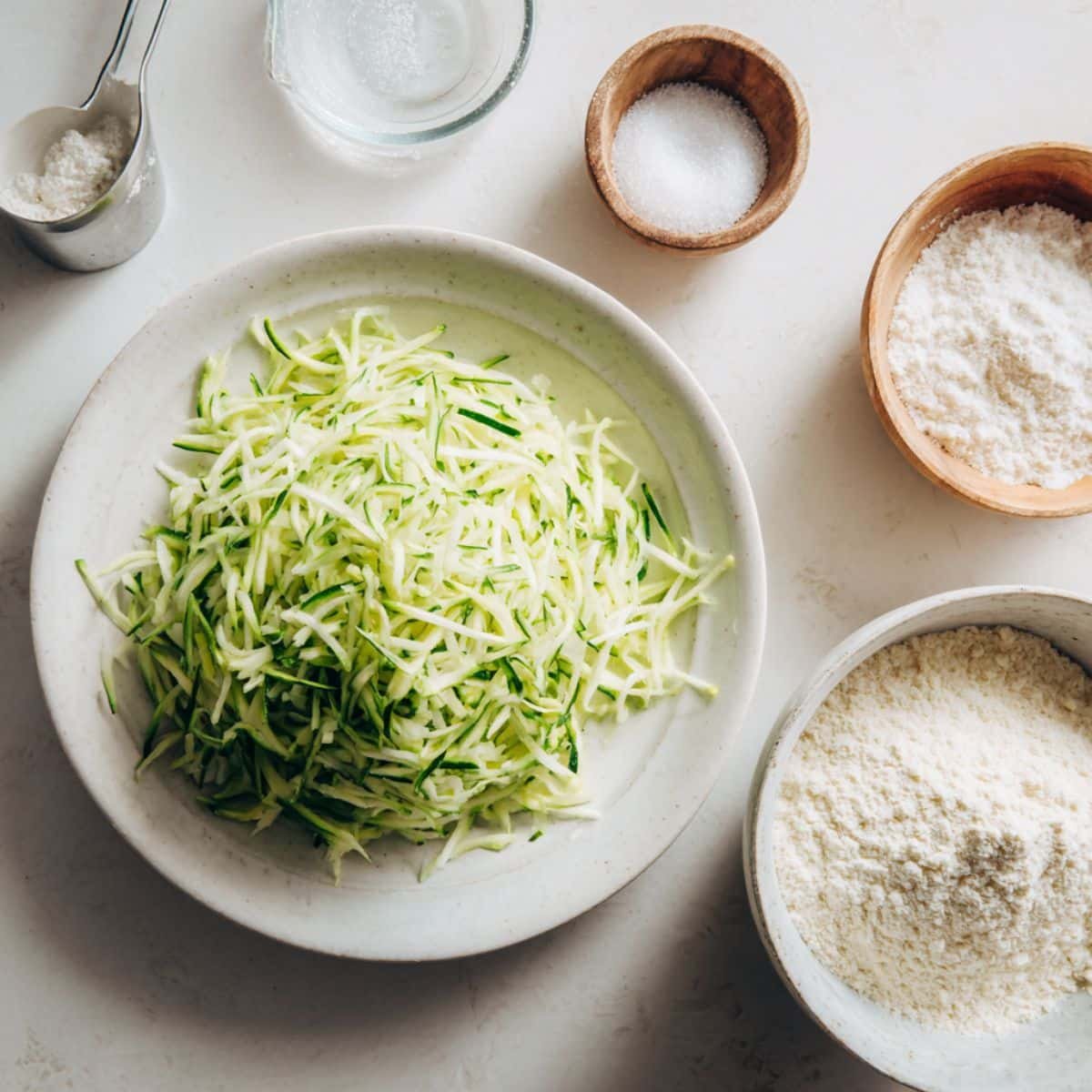 Grated zucchini and dry ingredients in mixing bowls