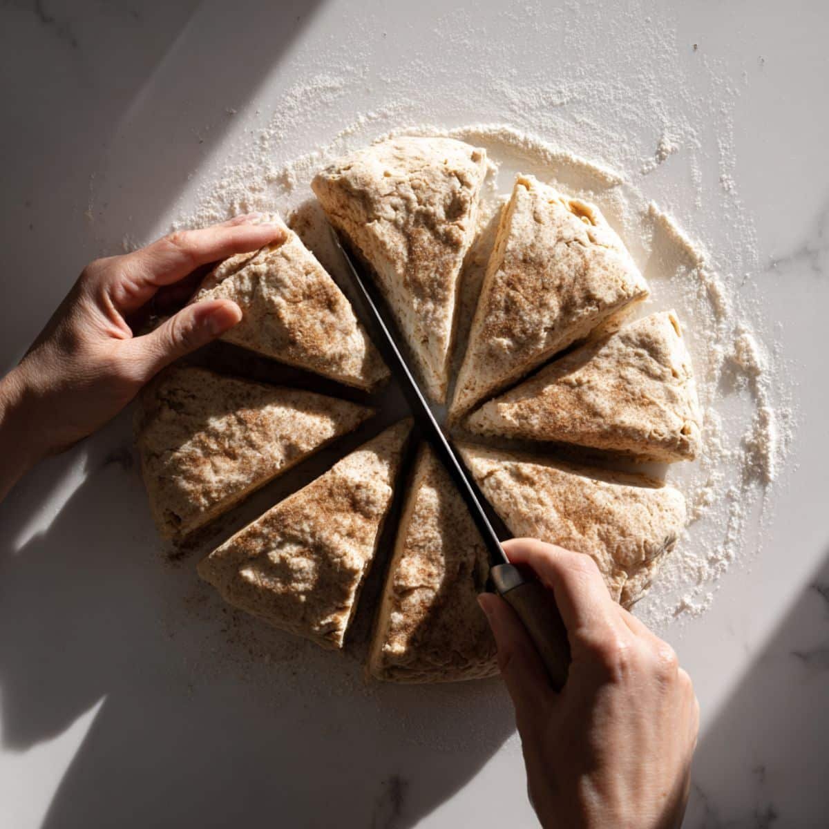 Shaping and cutting scone dough into wedges on a white floured surface	