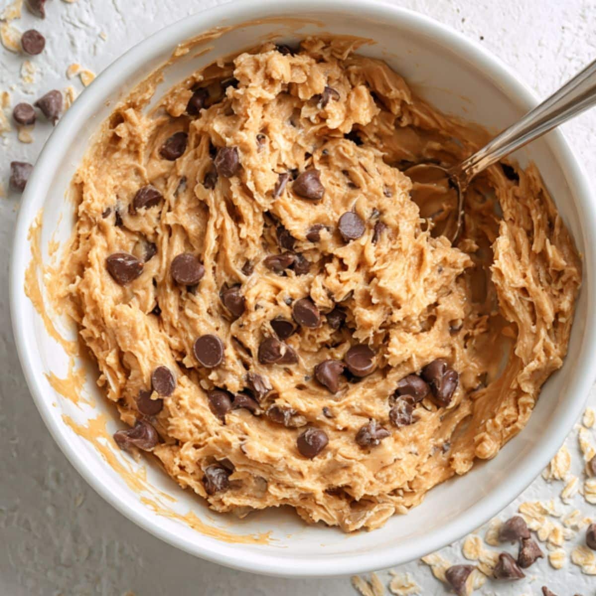 Sticky cookie dough with visible chocolate chips and oats in a white bowl	