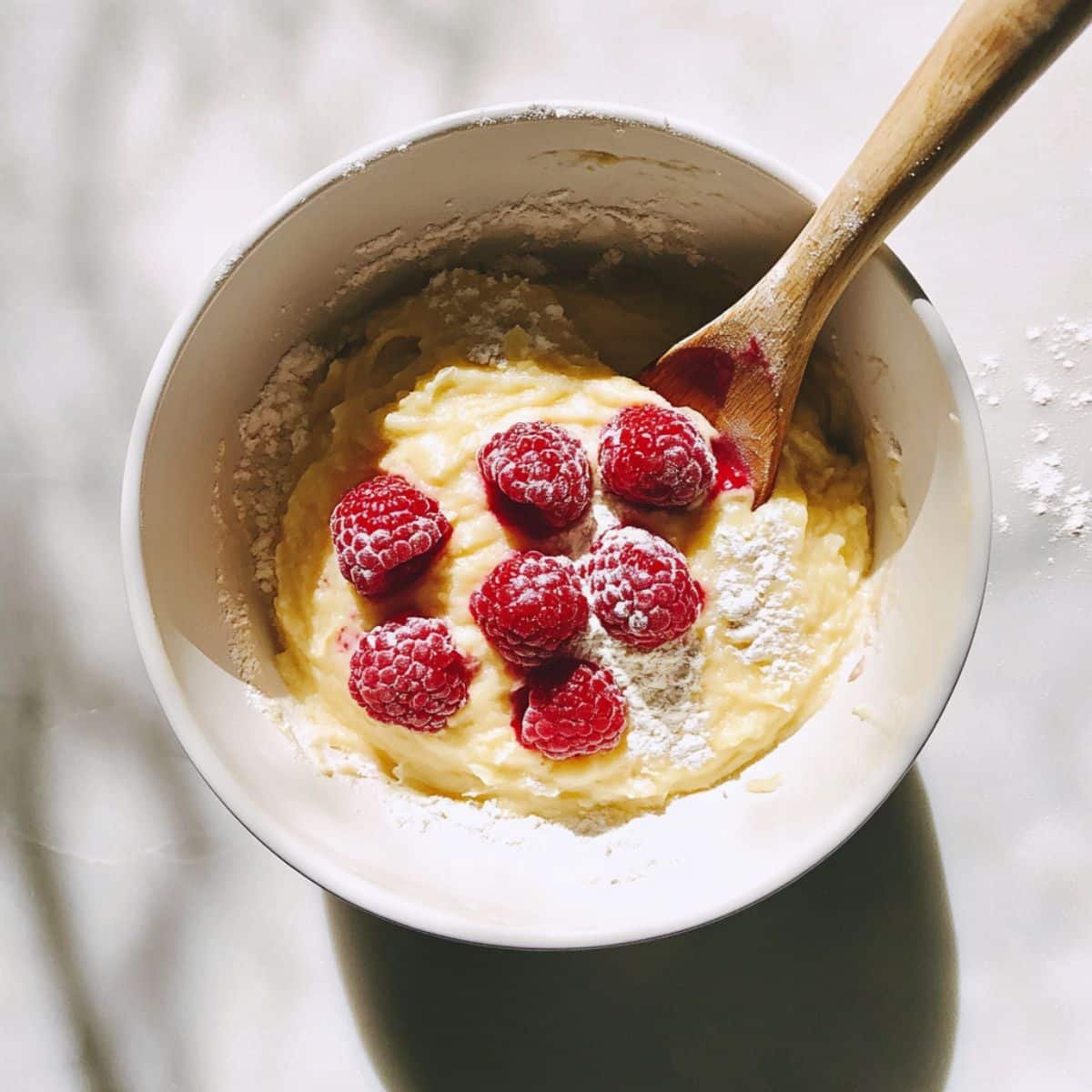 Folding raspberries into lemon cupcake batter in a white bowl	