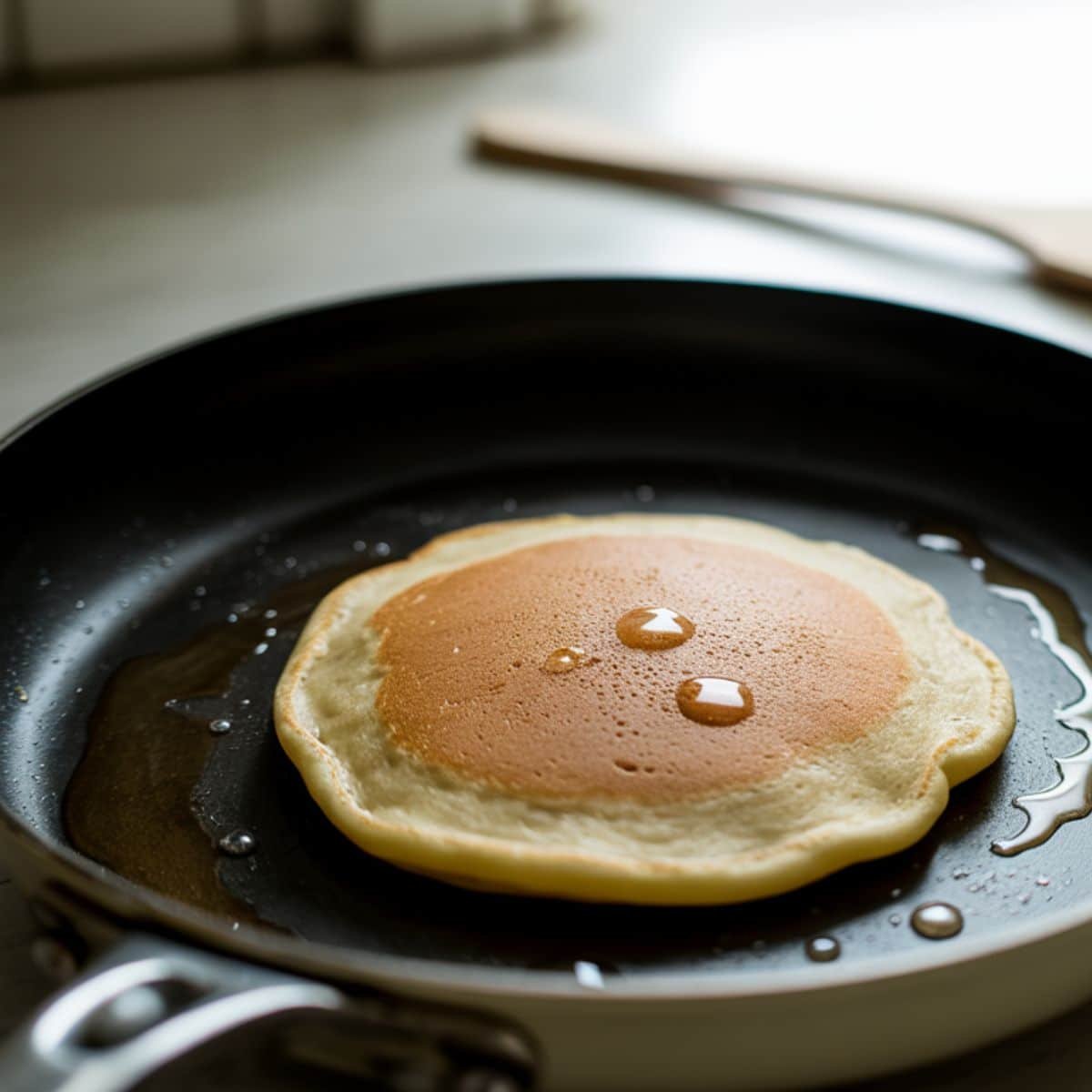 Almond flour banana pancake cooking with bubbles forming on skillet.	