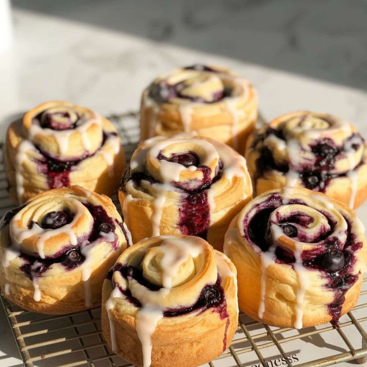 Freshly baked blueberry cruffins cooling on a wire rack with sugar glaze drizzled on top	