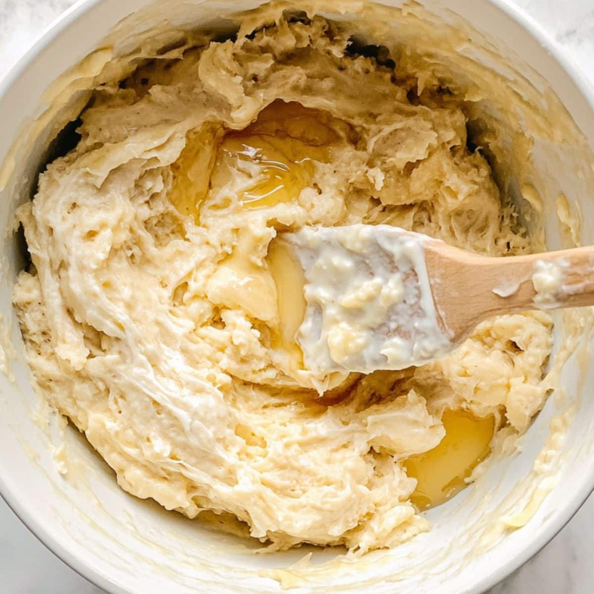Mixing mashed bananas, yogurt, eggs, and sweetener in a bowl on a white surface	