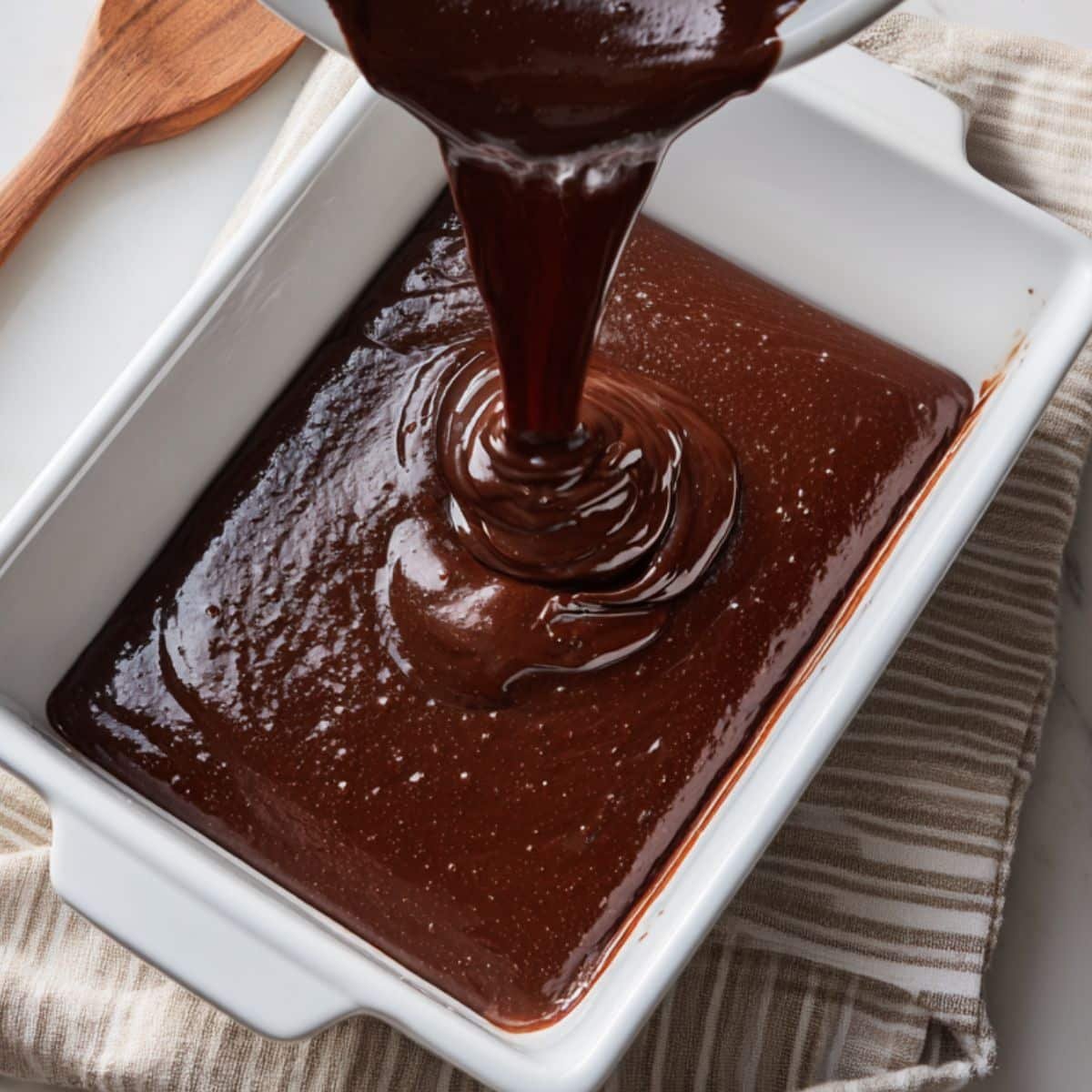 Chocolate batter being poured into a white baking pan	