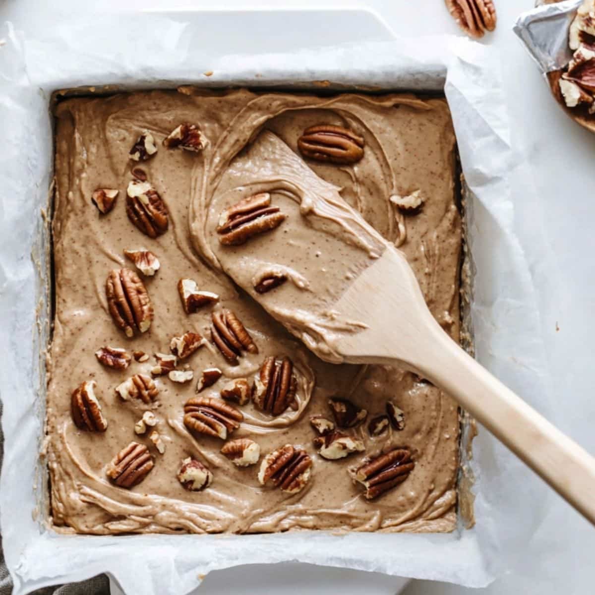 Folding chopped pecans into blondie batter in a white pan	