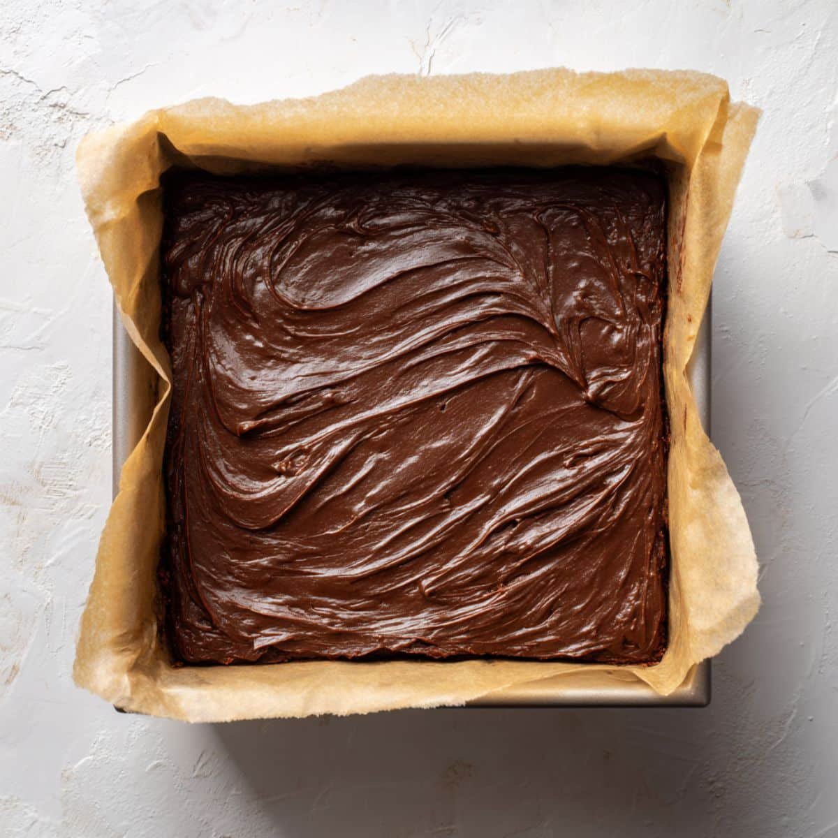 Unbaked brownie batter spread evenly in a parchment-lined pan	