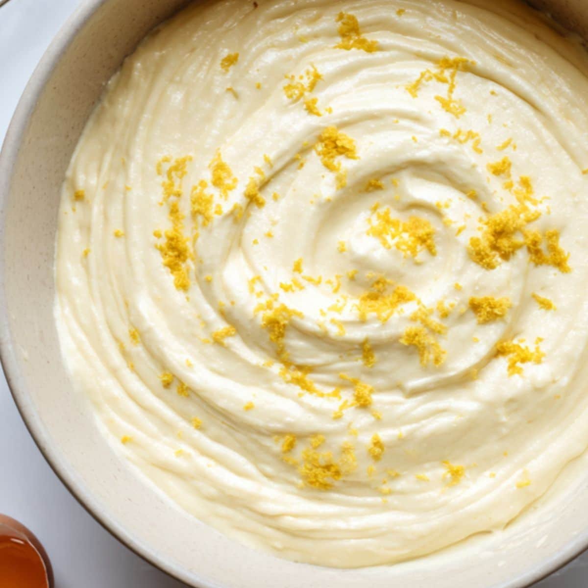 Creamy cheesecake batter being mixed with lemon zest and vanilla.	