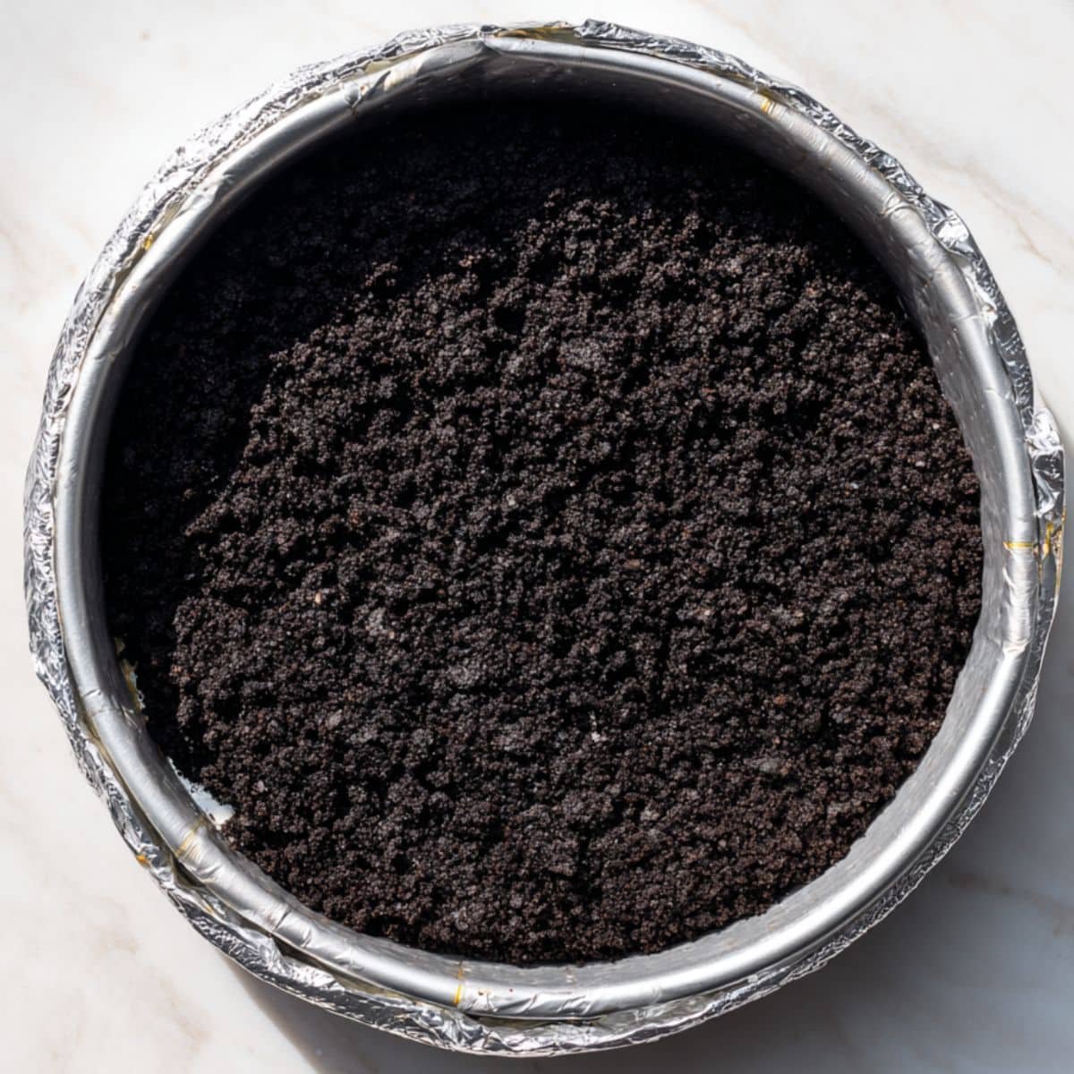 Pressing crushed Oreo crust into a springform pan on white countertop	