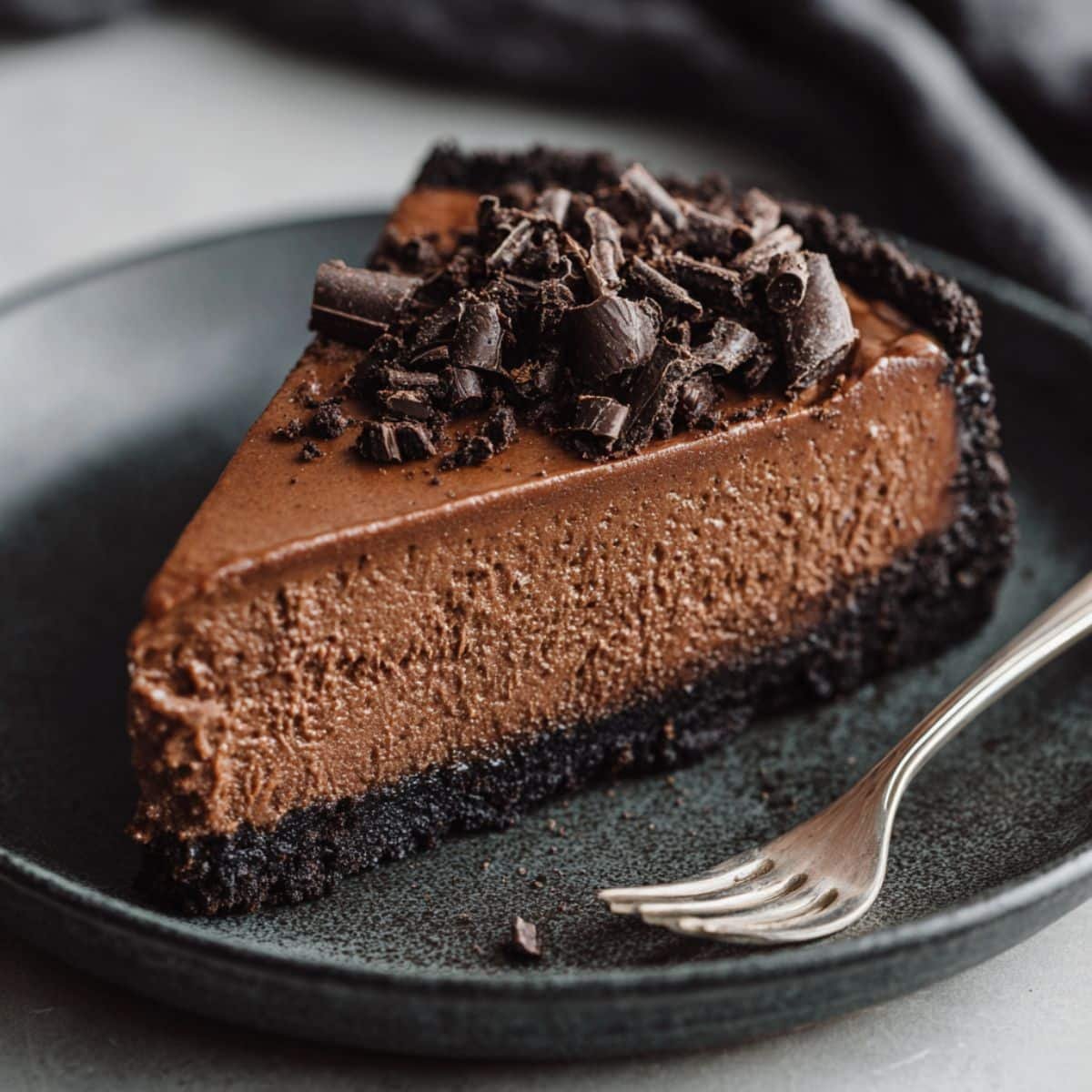 Slice of rich Chocolate Cheesecake Recipe with Oreo crust and chocolate shavings	