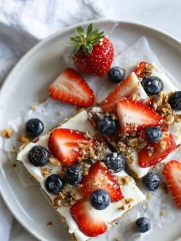 Homemade frozen yogurt bark topped with berries and granola on a white plate