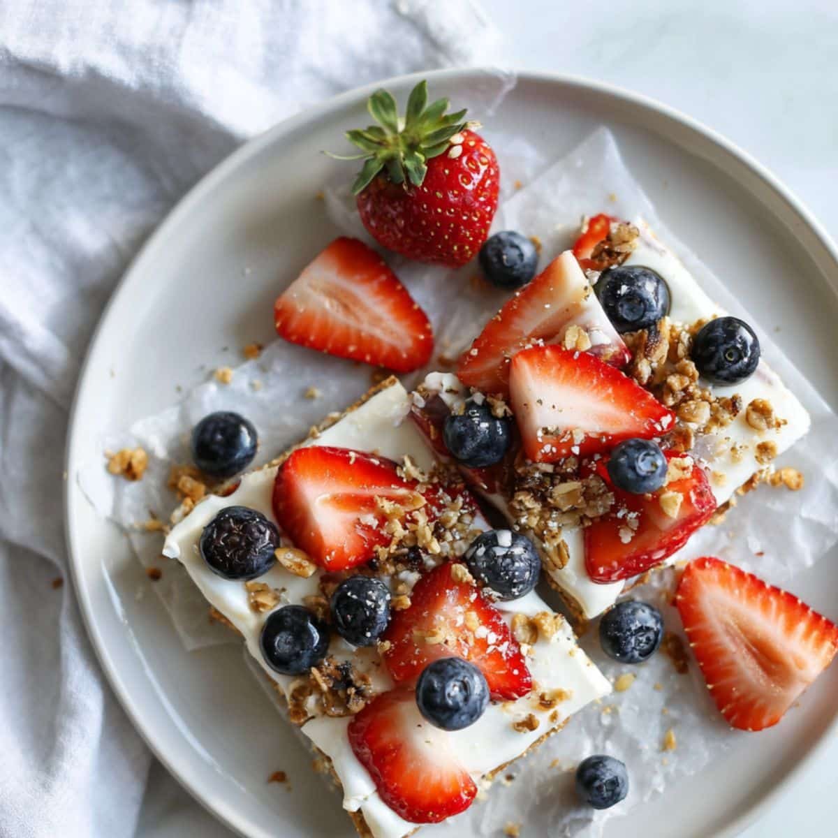 Homemade frozen yogurt bark topped with berries and granola on a white plate	