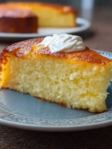 Slice of Greek yogurt cake with whipped cream on white plate