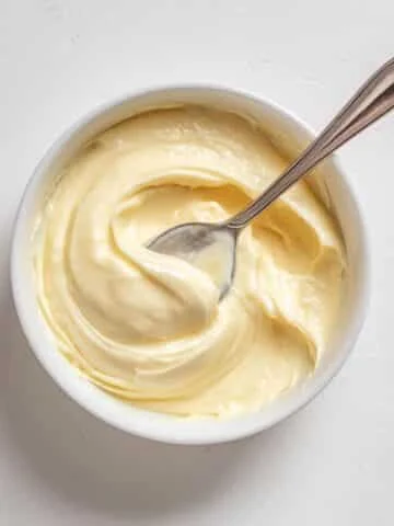 Spoon scooping homemade vanilla pastry cream from a bowl on a white counter