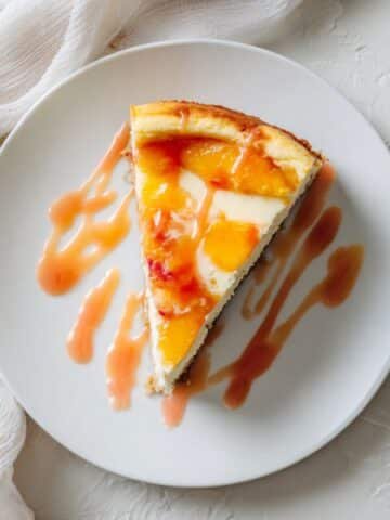 Homemade peach cheesecake slice drizzled with glaze on white counter