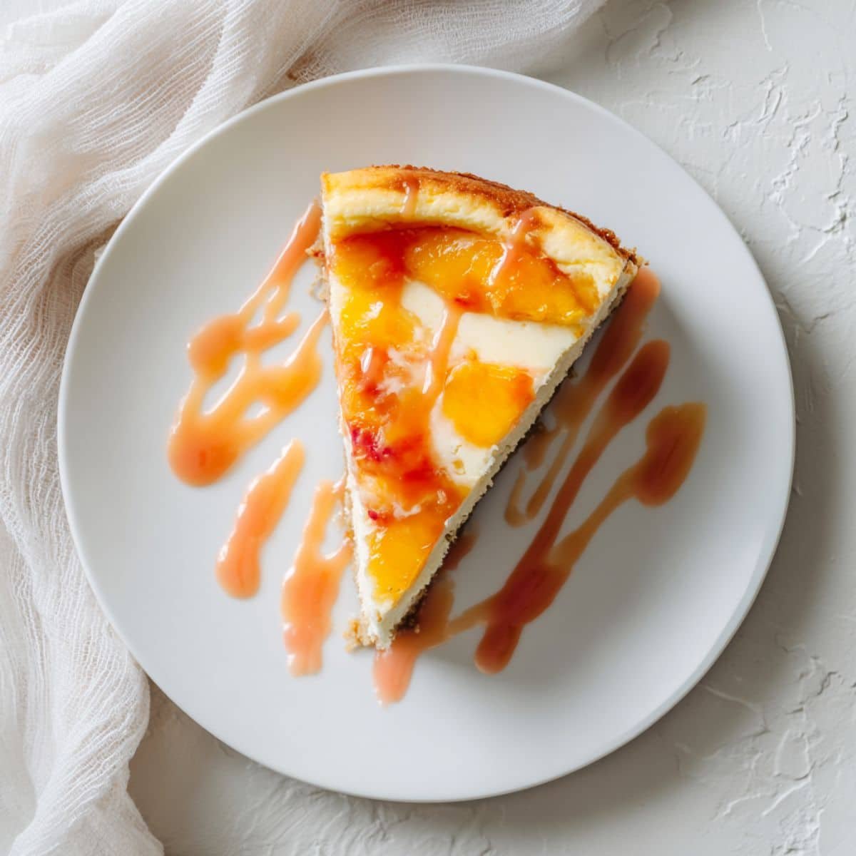 Homemade Peach Cheesecake Recipe slice drizzled with glaze on white counter	