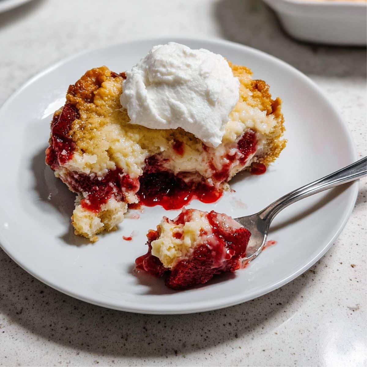 Top-down view of a rustic strawberry-cheesecake dump cake with a plated serving and whipped cream.	