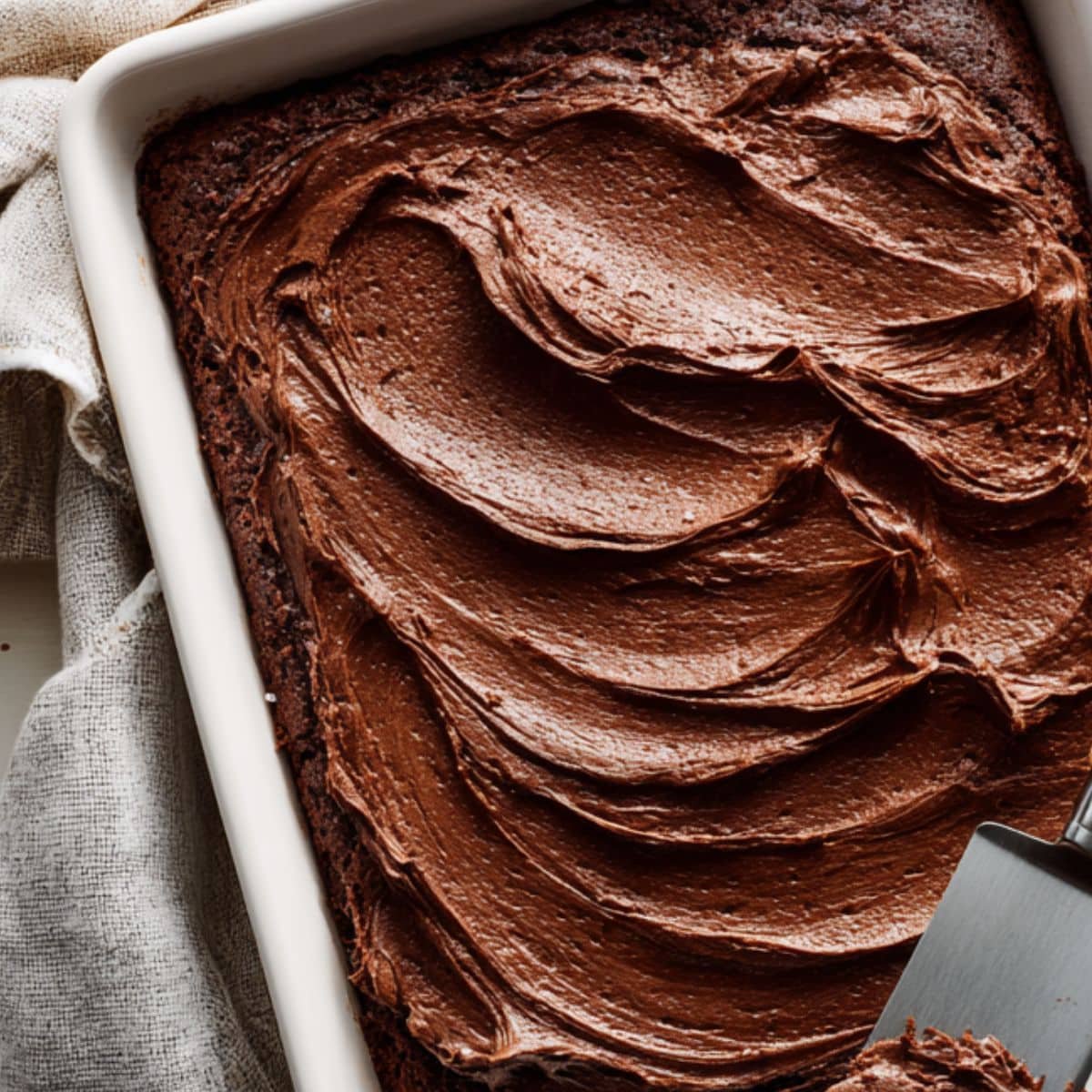 Freshly baked sheet cake being frosted with chocolate icing