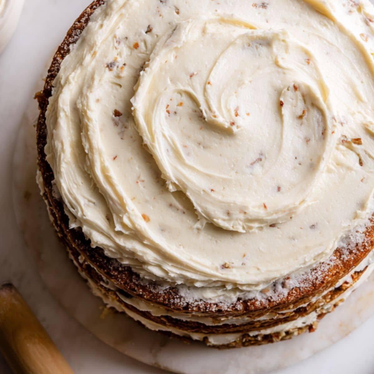 Hummingbird cake being assembled and frosted by hand on a white kitchen counter	
