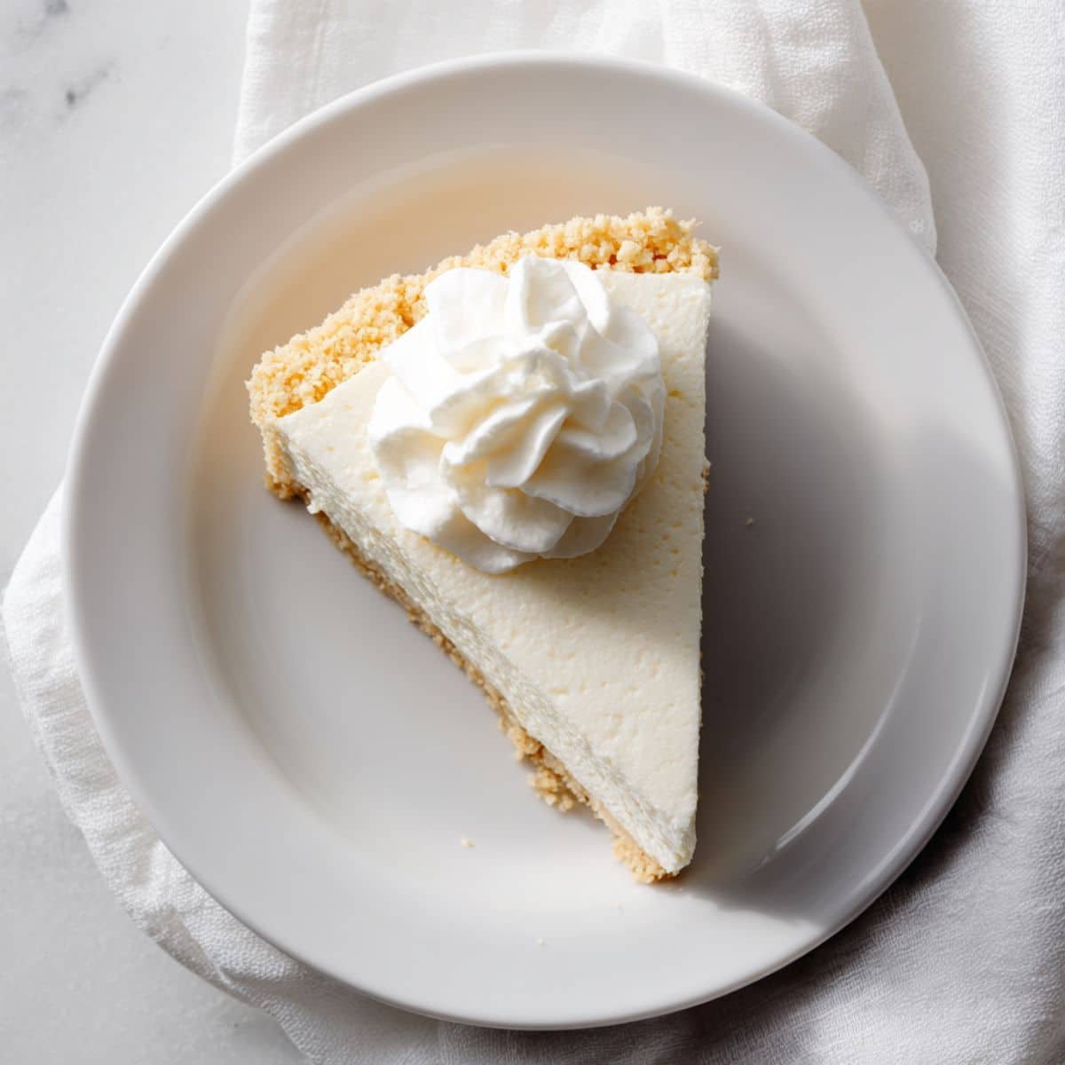 Slice of keto no bake cheesecake topped with whipped cream on a white plate	