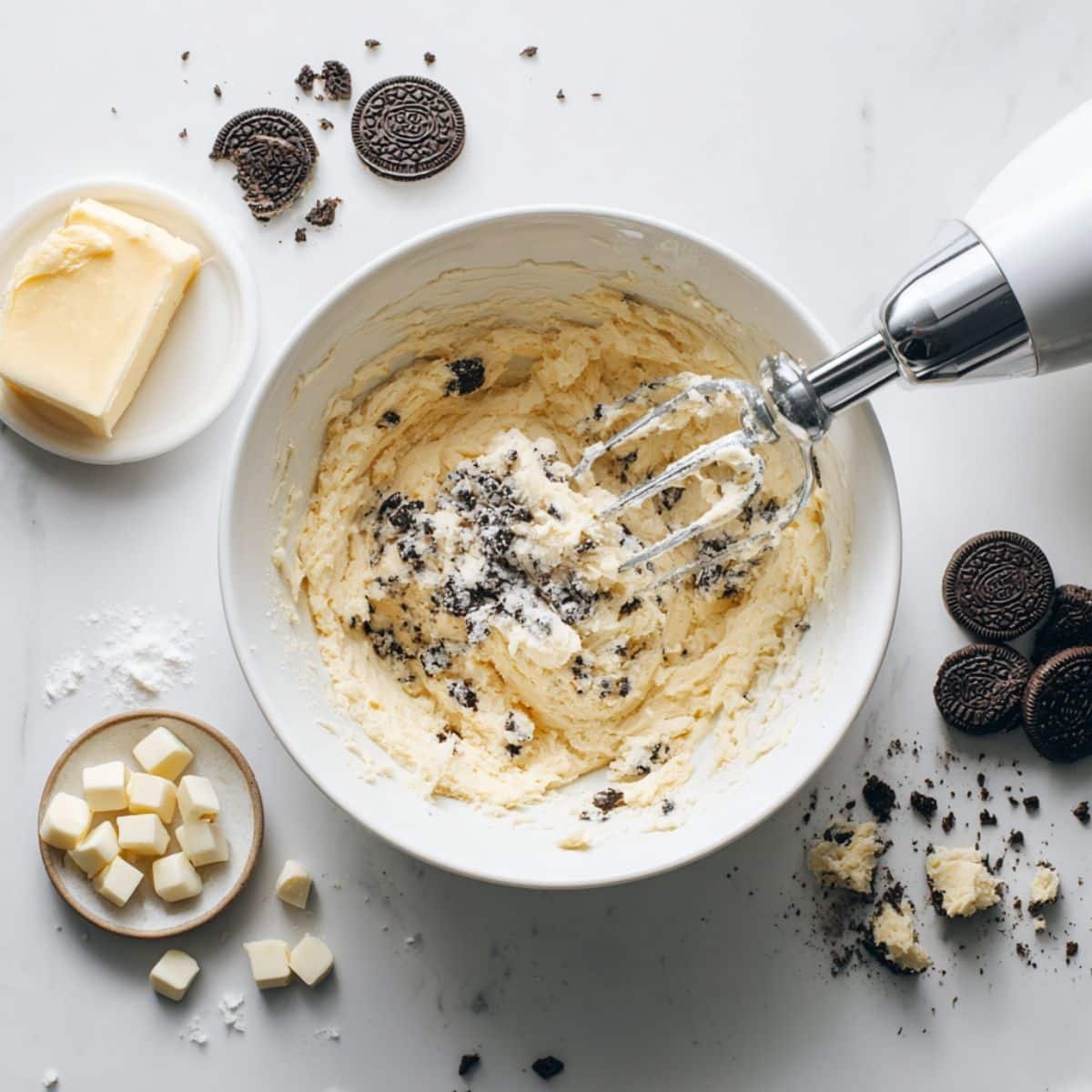 Creamed butter and sugar mixture in bowl with Oreos and chips nearby	