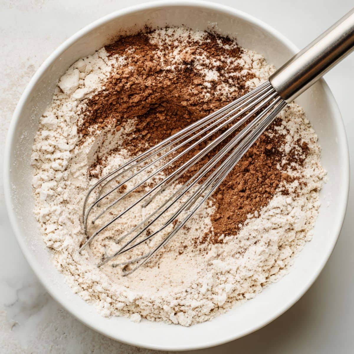 Flour, cocoa, sugar, and baking soda whisked in a white mixing bowl	