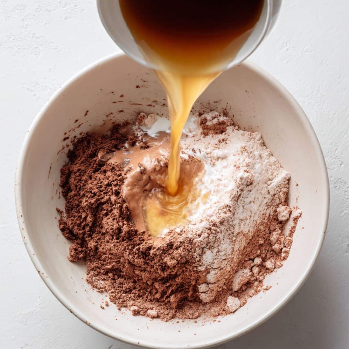 Wet ingredients being poured into dry ingredients in a mixing bowl	