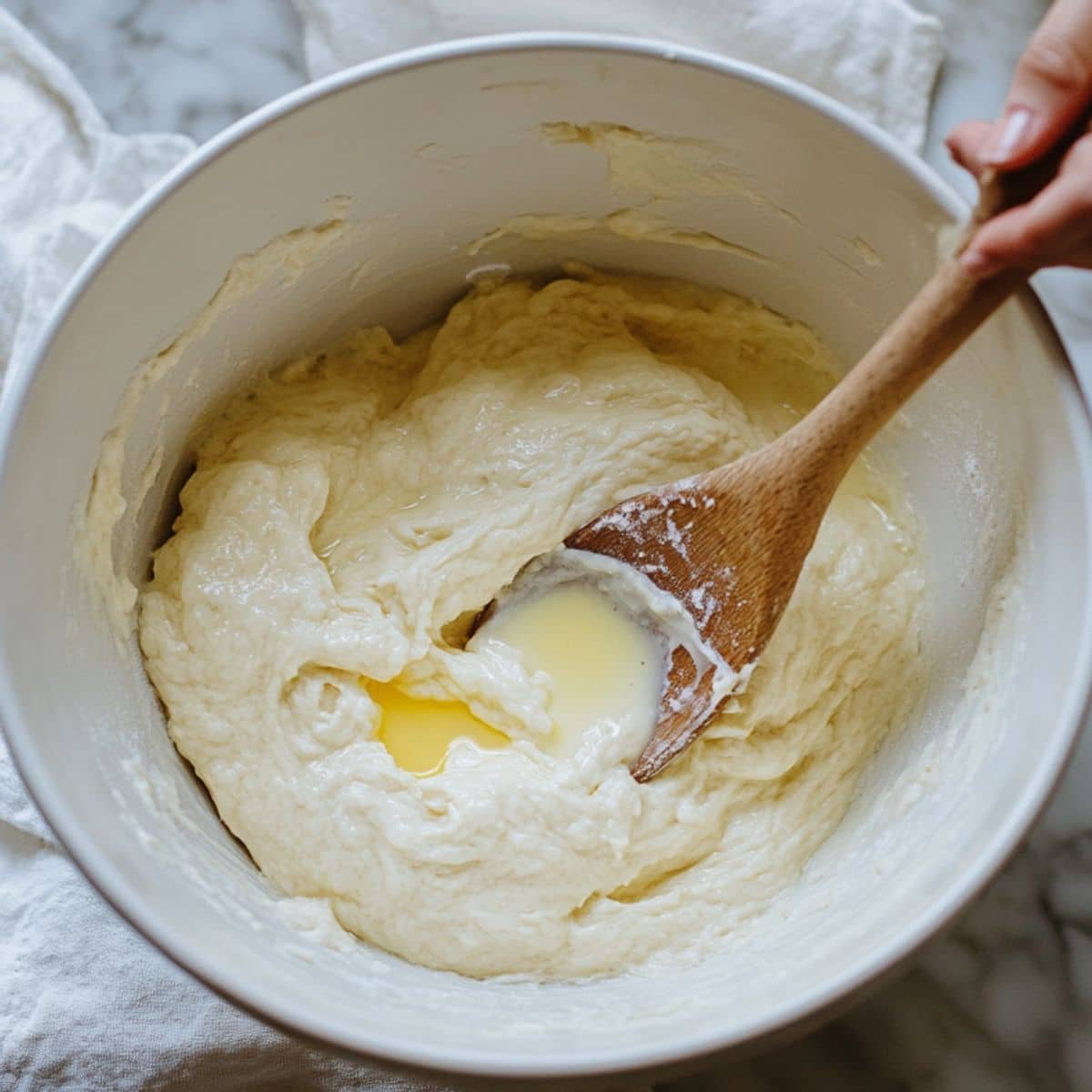 Home baker mixing dough in a white bowl with flour scattered around.	