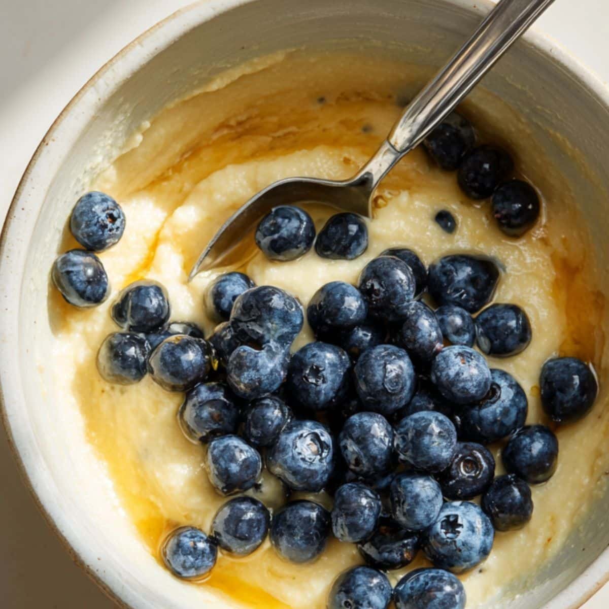 Mixing mashed banana, eggs, and blueberries in a bowl	