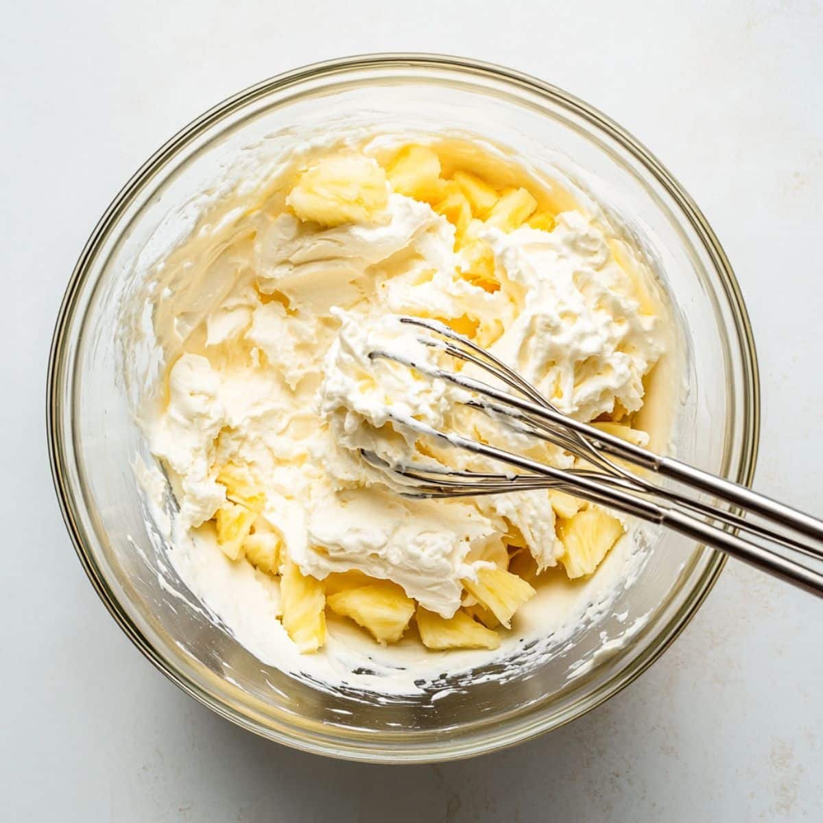 Whipped Cool Whip and pineapple frosting being mixed in a bowl	