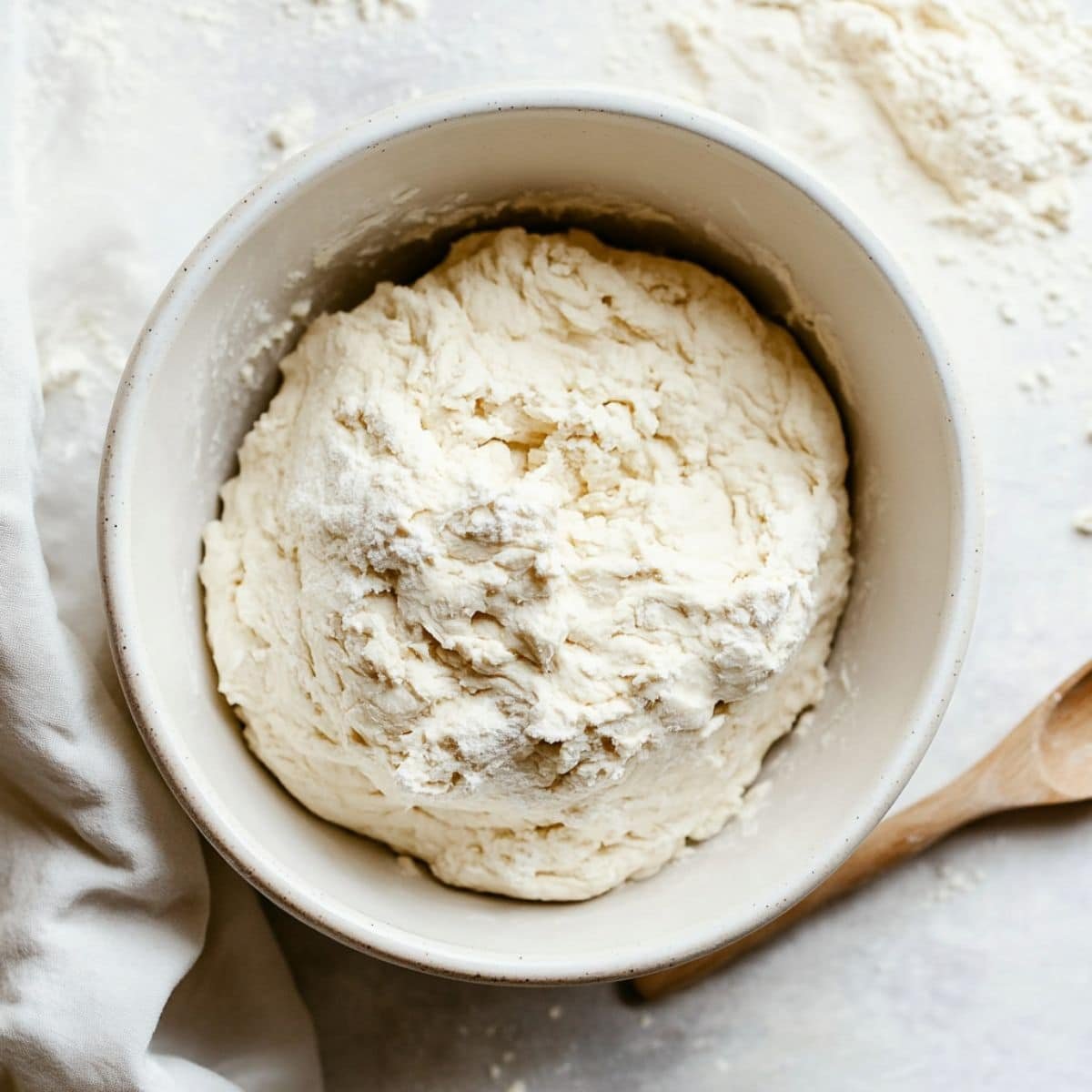 Mixing yeast dough for Belgian sugar waffles in a white bowl on a white counter	