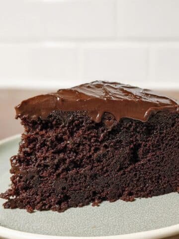 A slice of single layer chocolate cake with thick chocolate frosting on a white plate
