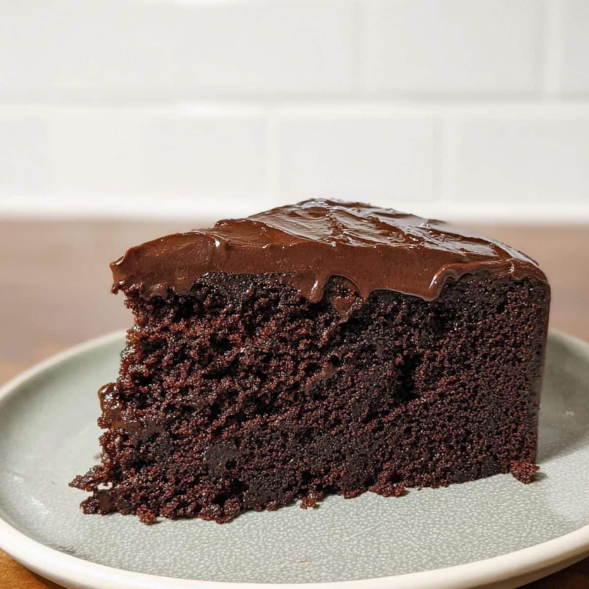 A slice of single layer chocolate cake with thick chocolate frosting on a white plate	